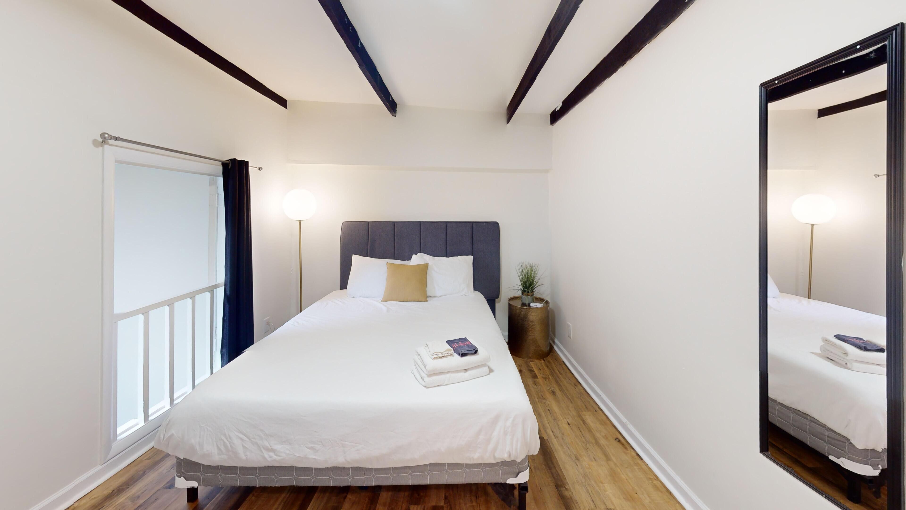 A neatly arranged hotel room with a large bed, a bedside lamp, a small potted plant, and a mirror on the wall.