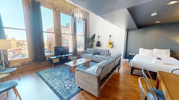 Una habitación de hotel moderna con un ventanal grande, un sofá, una cama, un televisor y una guitarra en la pared.