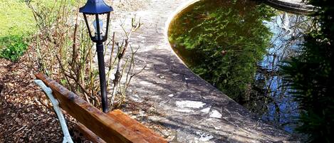 A wooden bench with a lamp post in a park with a pond.