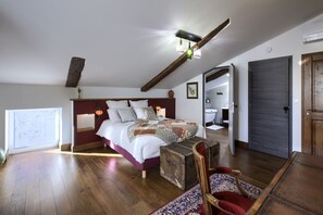Une chambre avec un grand lit, des poutres apparentes, une commode rustique et une vue sur la salle de bain.