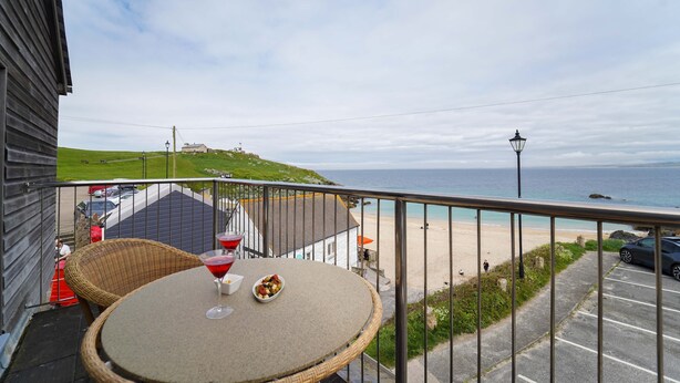 A balcony with a table, a wicker chair, and a view of the beach and ocean.