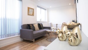 A modern living room with a grey sofa, a coffee table, and decorative items including two golden rabbit figurines. - Sunshine Place (Enfield)