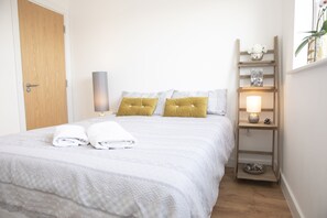 Un lit bien fait, recouvert d’une couvre-lit à motifs, avec deux oreillers et des serviettes pliées, le tout posé sur un plancher en bois.