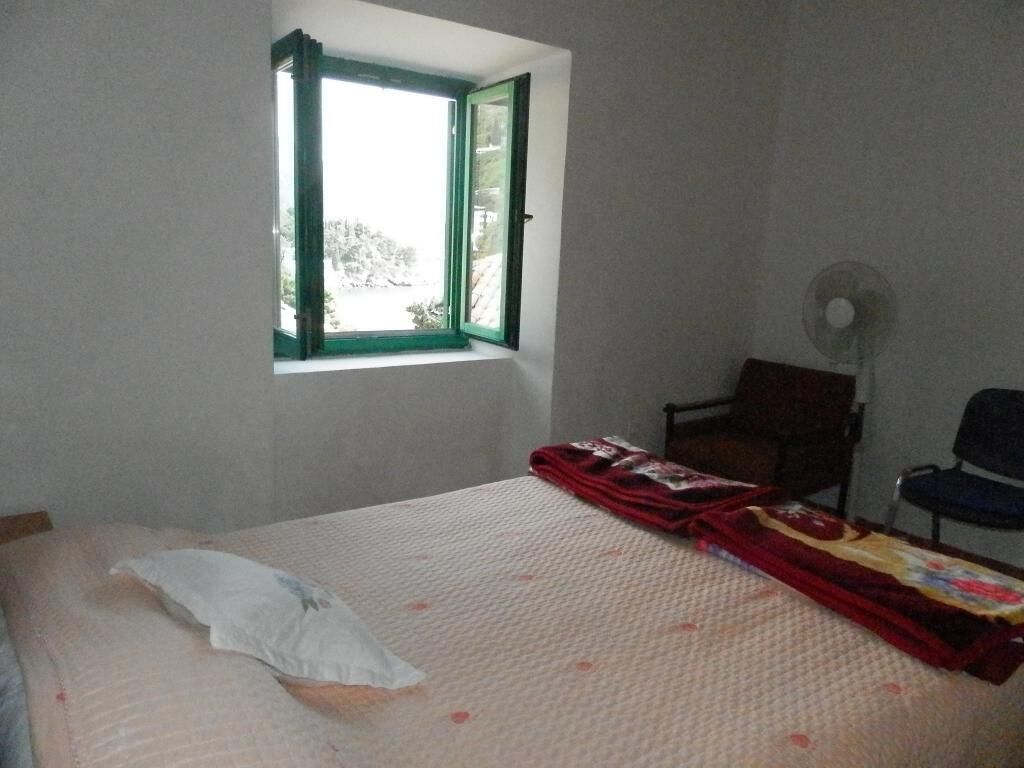 A bedroom with a bed, a window, a chair, and a fan.