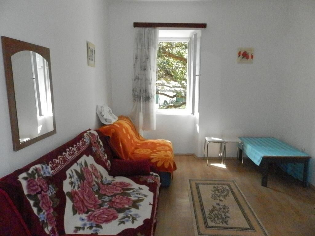 Une pièce avec un canapé à motifs floraux, une petite table, un banc et une fenêtre donnant sur des arbres.