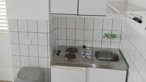 Et kompakt køkken med hvide skabe, en stålvask og en skraldespand.
