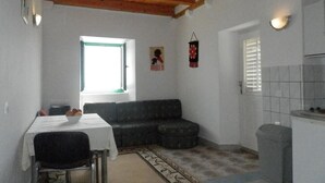 En kompakt opholdsstue med spisebord, sofa, lille vindue og et tekøkken.