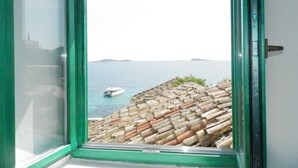 Et vindue med udsigt over et kystlandskab, med et tagtækket tag og en båd på vandet.