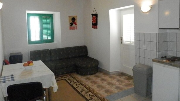 En kompakt opholdsstue med sofa, spisebord, lille tekøkken og et vindue med grønne skodder.