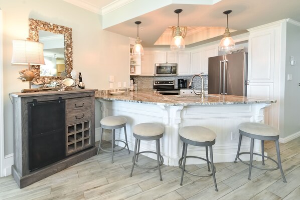 Una cocina con una isla grande, taburetes de bar, microondas y refrigerador.