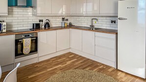 A modern kitchen with white cabinets, a stainless steel range hood, a built-in oven, and a white refrigerator. - 2 bedroom accommodation in Scarborough (Scarborough)