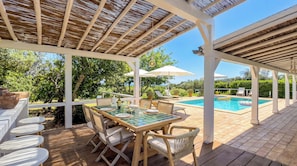 A covered outdoor area with a pool, wooden deck, and seating arrangements. - Cosy country house with heatable swimming pool and sea view. (Faro)
