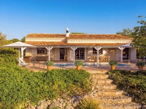 A two-story house with a tiled roof, a covered patio, and a swimming pool.