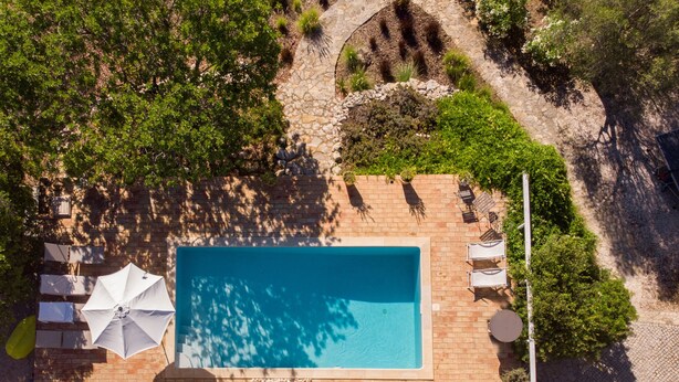 An aerial view of a rooftop swimming pool with a tiled deck, surrounded by greenery and a stone pathway. - Cosy country house with heatable swimming pool and sea view. (Faro)