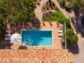 An aerial view of a rooftop swimming pool with a tiled deck, surrounded by greenery and a stone pathway. - Cosy country house with heatable swimming pool and sea view. (Faro)