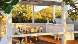 A wooden deck with a table and chairs, surrounded by white walls and a glass enclosure. - Cosy country house with heatable swimming pool and sea view. (Faro)