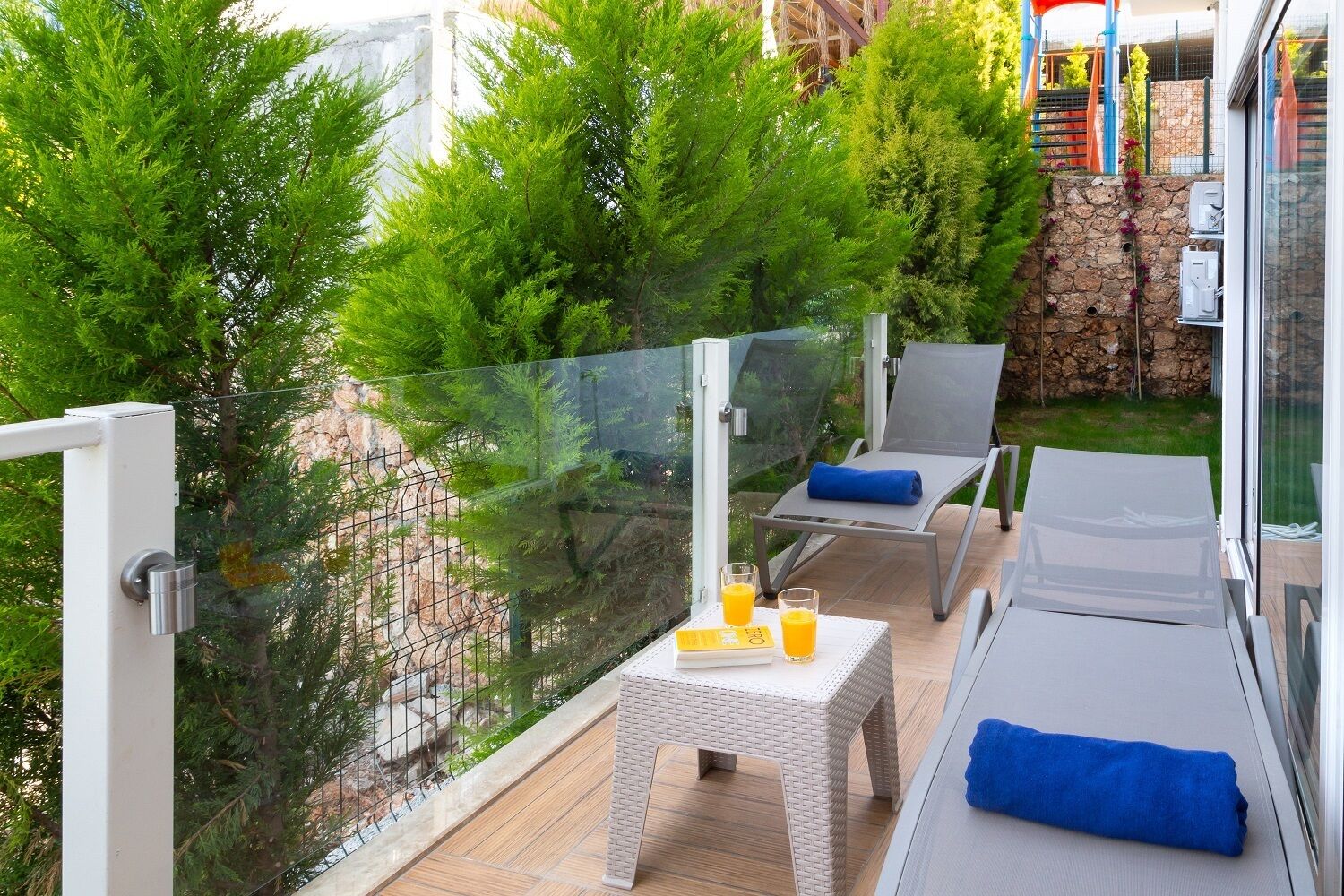 A balcony with a glass barrier, outdoor seating, and a small table with drinks.