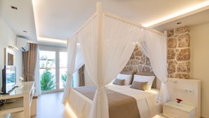 A modern bedroom with a four-poster bed, a stone accent wall, and a TV on a desk.