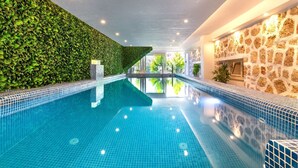 An indoor swimming pool with tiled walls, a green leafy wall on one side, and a stone wall on the other.