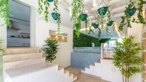 A modern interior with a staircase leading to a living area, a kitchen in the background, and hanging plants.