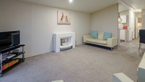 Ein Wohnzimmer mit Fernseher, Sofa, Kamin und einem zur Küche hin führenden Gang.