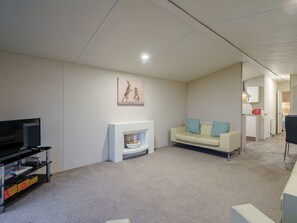 A living room with a TV, sofa, fireplace, and a hallway leading to a kitchen. - The Paddocks - UK7112 (Dollar)