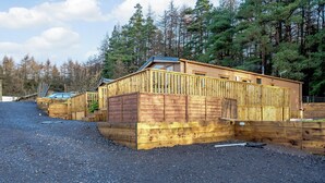Eine Holzhütte mit geneigtem Dach, umgeben von einer Schotterauffahrt und an einen bewaldeten Bereich angrenzend.