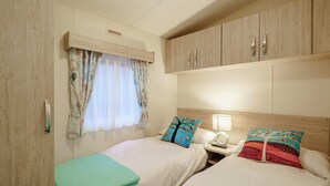Ein Schlafzimmer mit zwei Betten, einem Fenster mit Vorhängen, einem Nachttisch mit Lampe und Holzschränken.