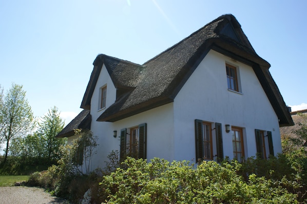 A white house with a steeply pitched roof and green shutters, surrounded by greenery. - Thatched-Roof Vacation Home Right on the Baltic Sea (Schwarzer Busch / Insel Poel)