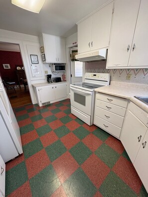 A compact kitchen with white cabinets, a microwave, a stove, and a checkered floor pattern.
