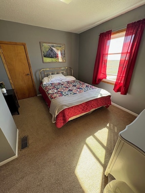 Ein Schlafzimmer mit einem Bett, einer T ür, einem Fenster mit roten Vorhängen und einem Bild an der Wand.