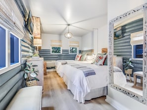 Un dormitorio con una cama grande, mesitas de noche, un espejo y un ventilador de techo.