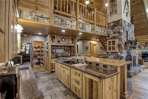 Une cuisine spacieuse avec des meubles en bois, un grand îlot central et une cheminée en pierre.