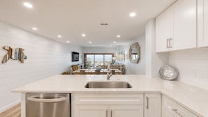 A kitchen with a large island, white cabinetry, and a view to the living area. - Updated Two Bedroom Fourth Floor Captains Walk Condo, Oceanfront Views (Hilton Head)