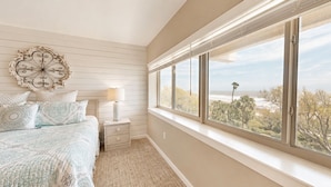 A bedroom with a bed, bedside table, lamp, and a large window with a view of the outdoors. - Updated Two Bedroom Fourth Floor Captains Walk Condo, Oceanfront Views (Hilton Head)
