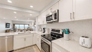 A modern kitchen with white cabinetry, a stainless steel microwave, a black stove, and a toaster. - Updated Two Bedroom Fourth Floor Captains Walk Condo, Oceanfront Views (Hilton Head)