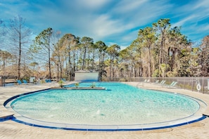 Piscina clara rodeada por uma vedação, com árvores e uma área coberta ao fundo.