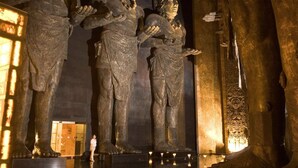 A series of ancient stone statues in a dimly lit room with a reflective floor.