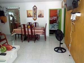 A dining area with a table and chairs, a fan, and a small bed in the background. - Room-green Sea Inn, San Luis With View o (San Andrés)