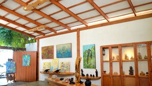 A covered outdoor area with wooden beams and a tiled floor, featuring artwork and decorative items on the walls and shelves. - Galería Suites San Pancho (San Francisco)