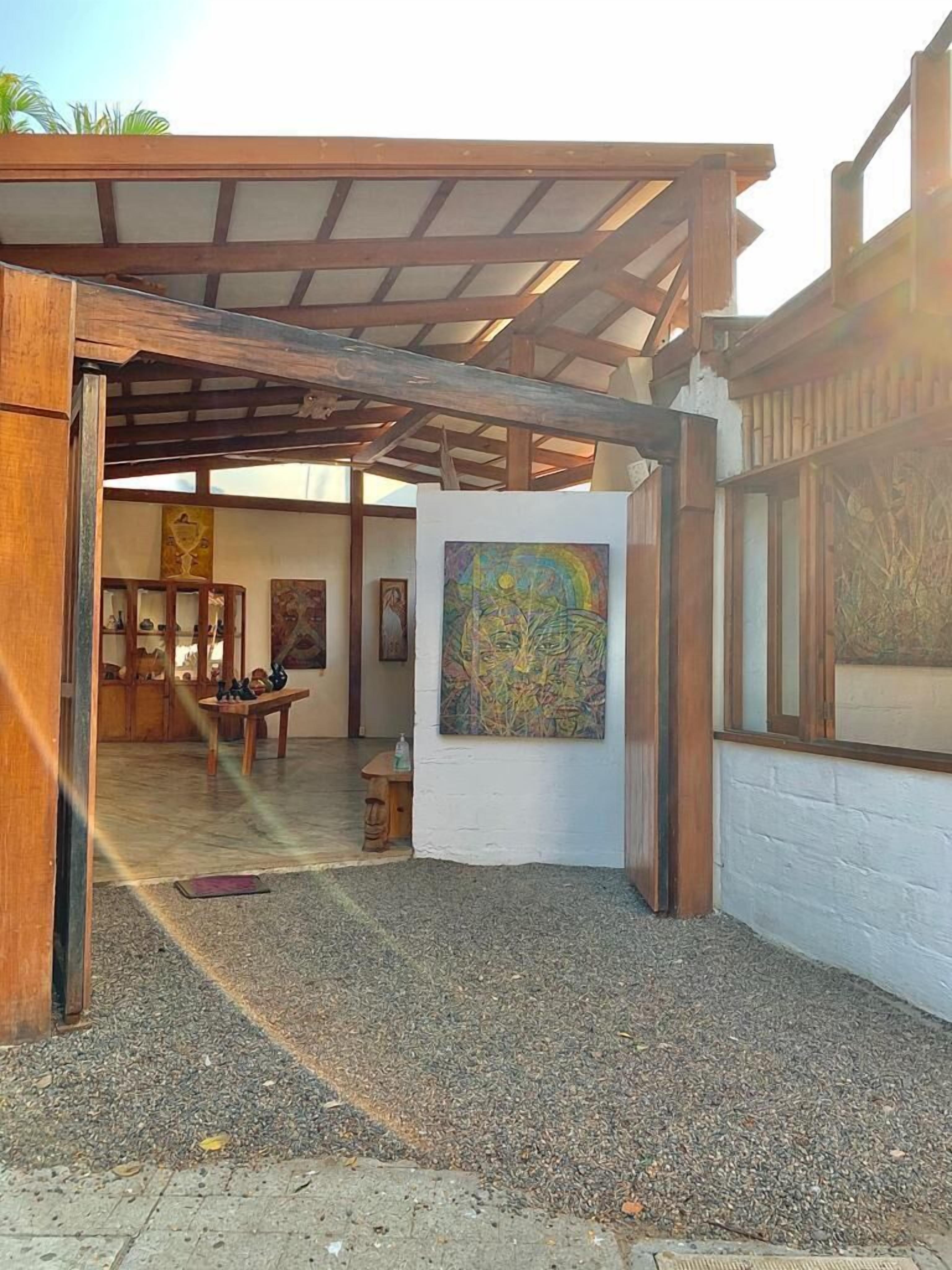 Una galería al aire libre con una pérgola de madera, un cuadro abstracto de gran tamaño y una exhibición de esculturas.