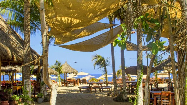 A beachside restaurant with outdoor seating, palm trees, and a view of the ocean. - Galería Suites San Pancho (San Francisco)