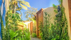 A narrow pathway leading to a building with a statue on the right. - Galería Suites San Pancho (San Francisco)