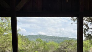 A room with a checkered floor, wooden walls, and a large window offering a view of a green landscape with trees and hills. - Concan Frio River Cabin (Concan)
