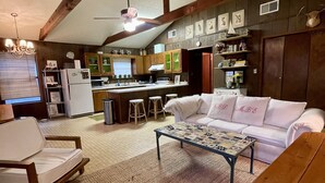 A spacious living area with a high ceiling, wooden beams, a white sofa, a patterned coffee table, and a kitchen in the background. - Concan Frio River Cabin (Concan)