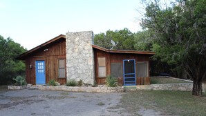A rustic cabin with a stone chimney, a blue door, and a satellite dish. - Concan Frio River Cabin (Concan)