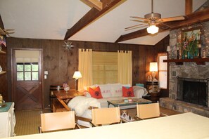 A cozy room with a fireplace, wooden walls, a ceiling fan, and a dining area with chairs and a table. - Concan Frio River Cabin  (Concan)