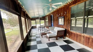 A covered porch with a checkered floor, wooden walls, and a ceiling fan. - Concan Frio River Cabin (Concan)