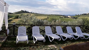 Una terraza con sillones blancos que dan a un paisaje de viñedos.