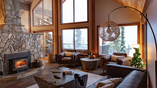 A cozy living room with a stone fireplace, large windows, and comfortable seating. - Big White Is Calling -  Big White BC (Beaverdell)
